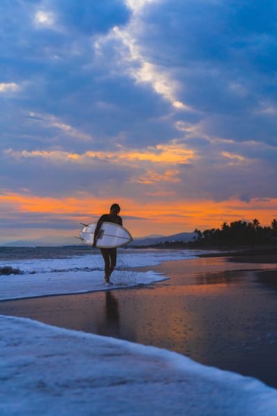 Woman surfer with surfboard on the ocean at sunset.